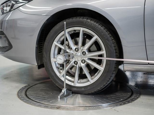 A car's front wheel on a turn plate with a mechanical caster-camber gauge clamped to the hub
