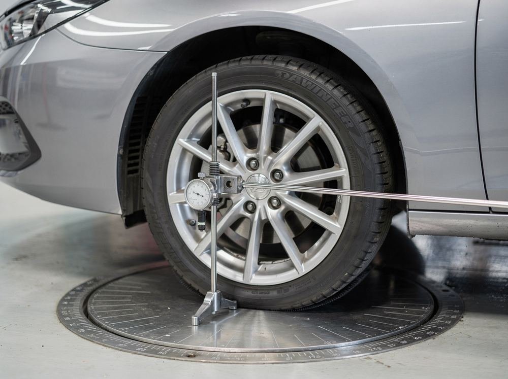 A car's front wheel on a turn plate with a mechanical caster-camber gauge clamped to the hub