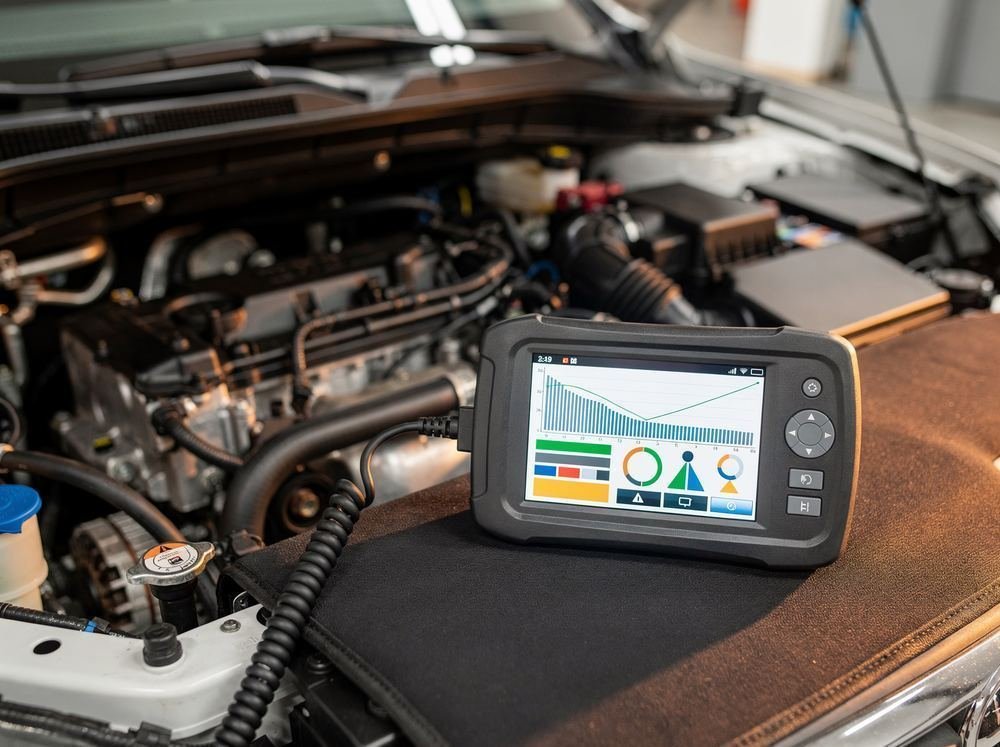 Diagnostic scan tool resting on the fender of an open engine bay, its screen showing a diagnostic readout with graphs and status indicators